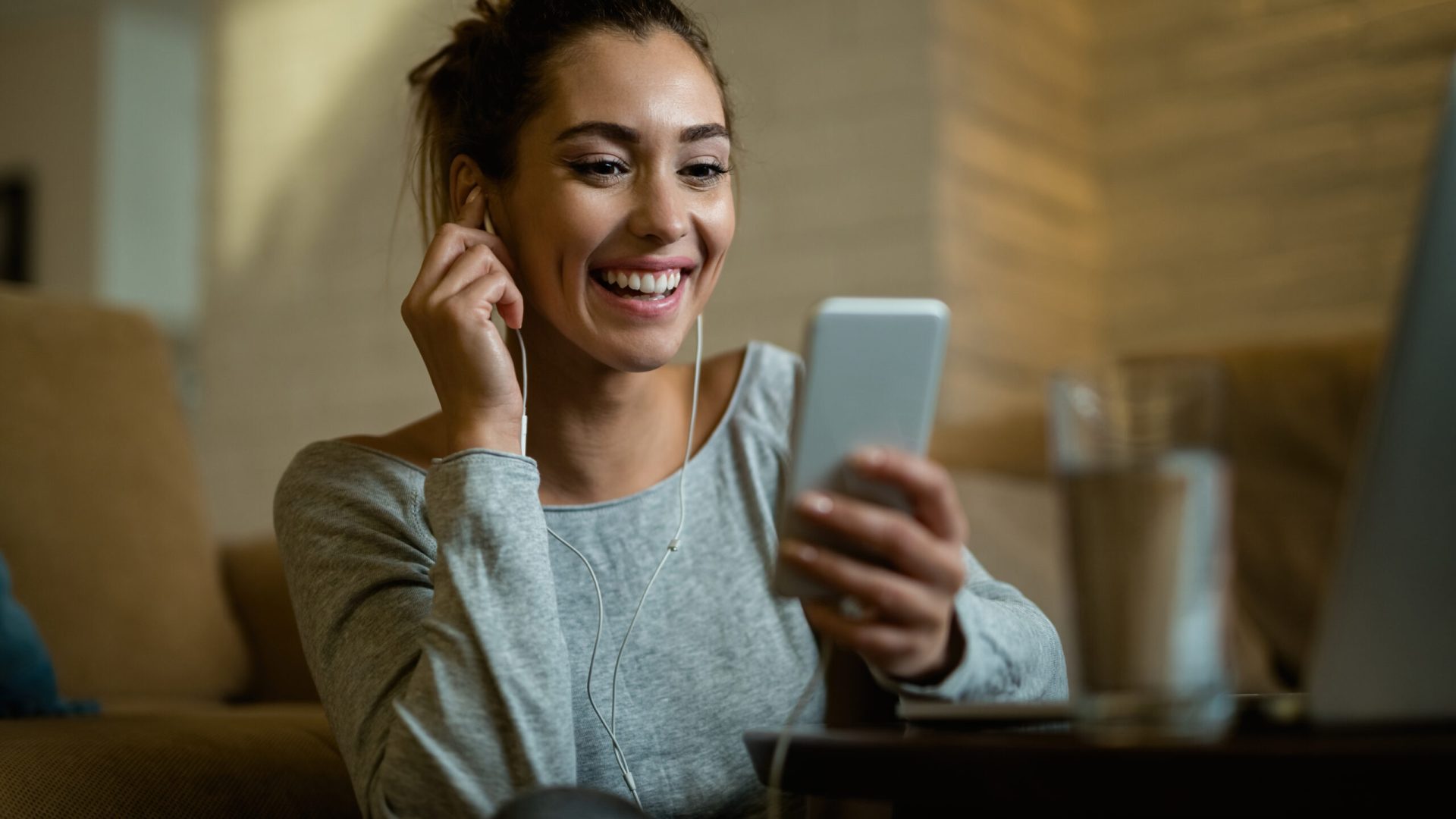 Young happy woman having fun while using mobile phone and reading text message in her living room.