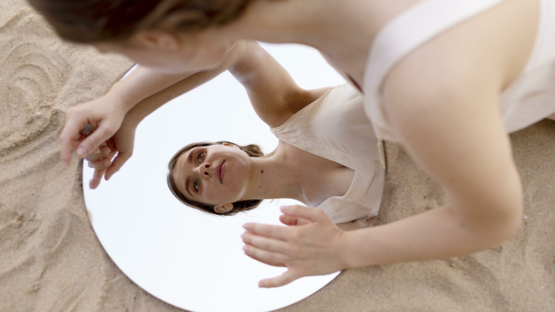 young-woman-posing-outdoors-beach-using-round-mirror